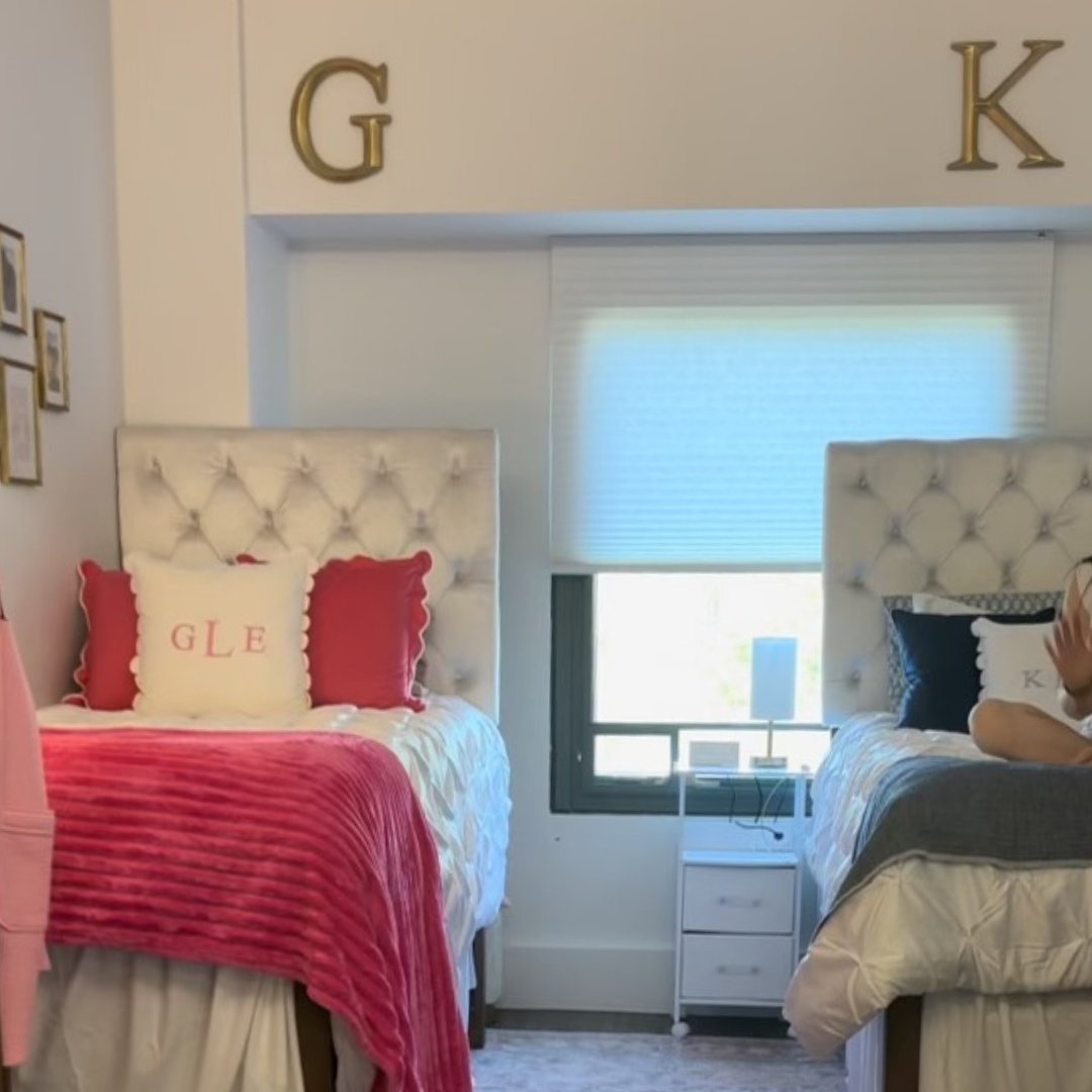 Two beds one with red and white linens and initials on pillow the other with black and white linens and pillow with initials