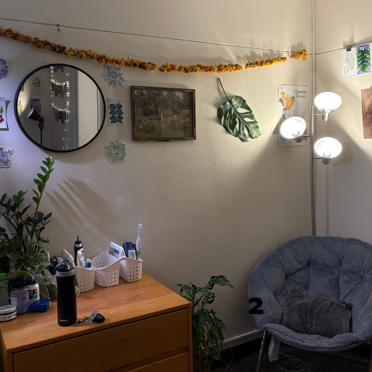 A cozy, dimly lit residence hall room corner featuring a wooden dresser, a plush chair, and nature-themed wall decor