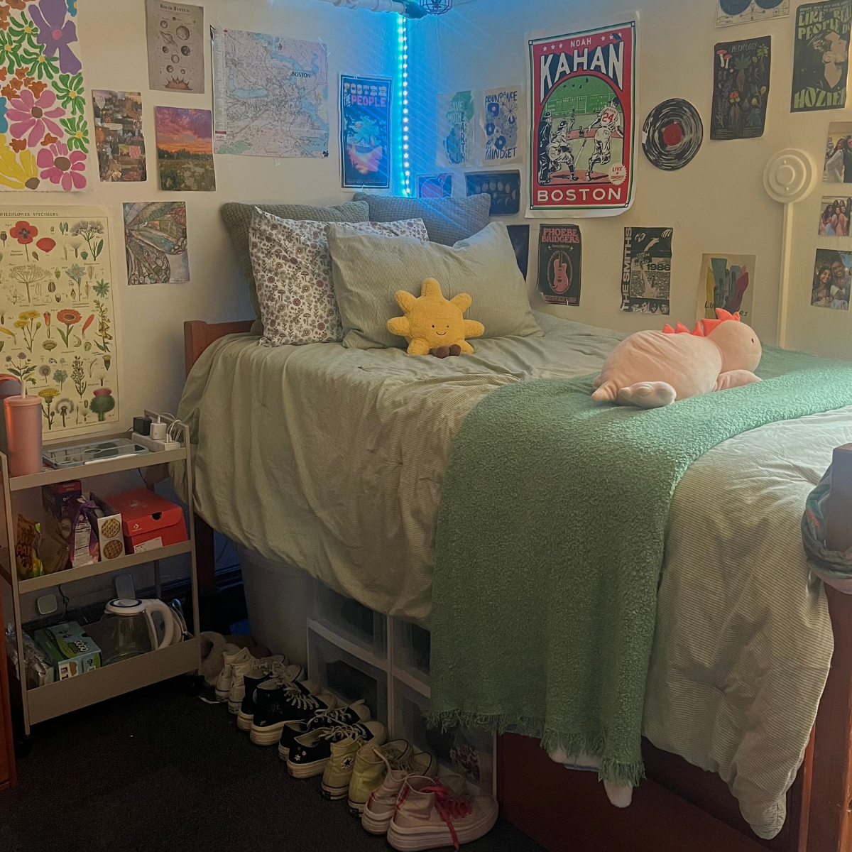 A bed in a residence hall room covered in sage green bedding, decorated with a gallery wall of posters and art, and illuminated by blue LED lights