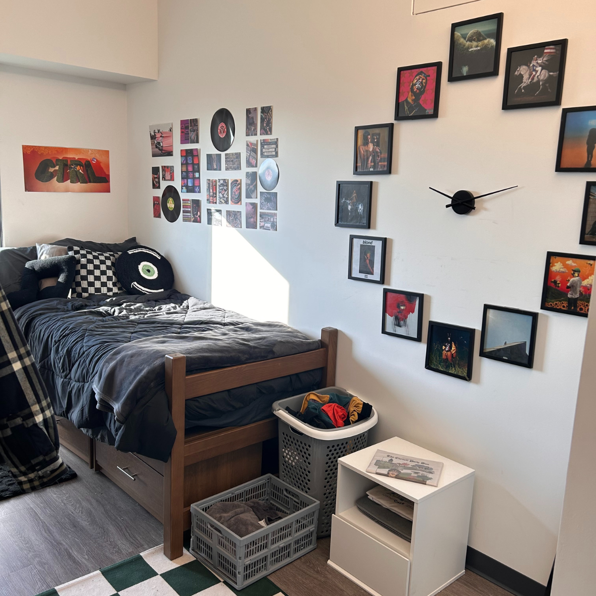 Residence hall room with a bed and blue comforter pictures on the wall in a circle used as hours for a clock green and white checkered rug