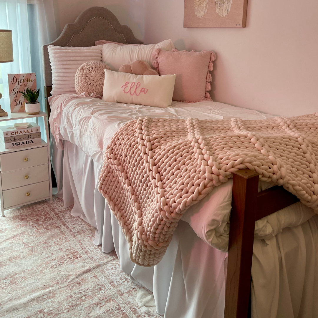 Student room picture of bed with afghan, pillow with name, nightstand with lamp