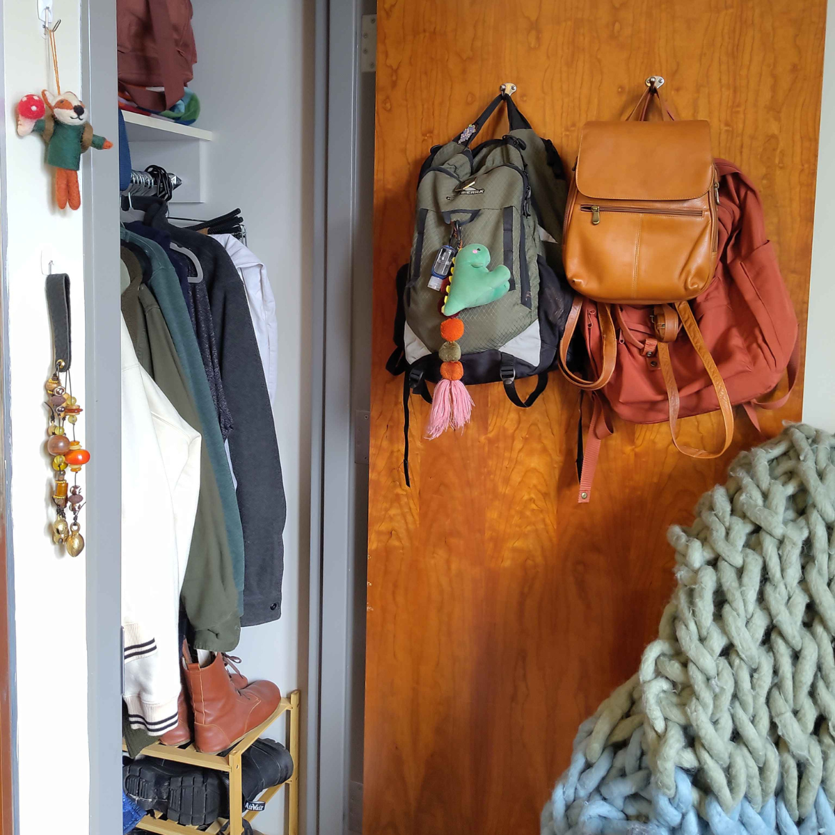 Residential room backpack and purse hanging on the back of door closet with clothes hanging on hangers and shoe rack