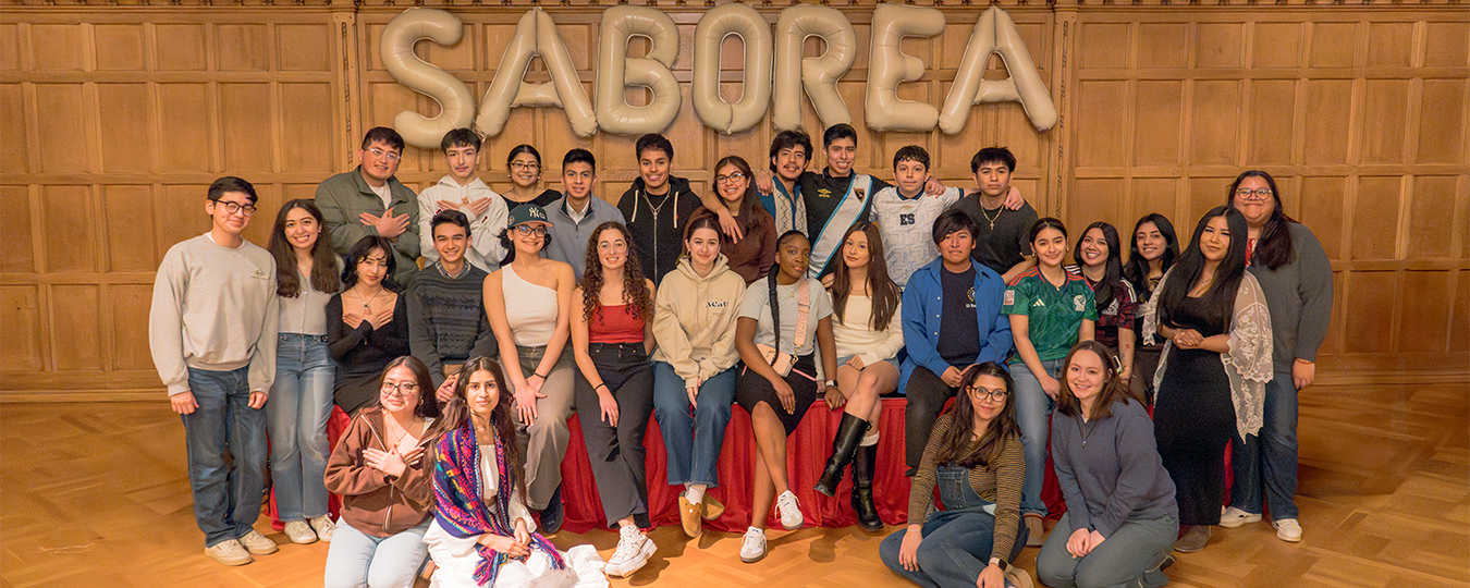 Student pose in front of balloon letters that spell out "SABOREA"