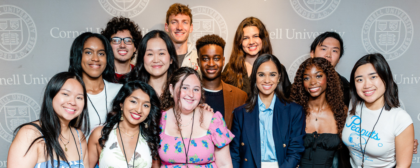 Group of students smiling together in front of a Cornell backdrop