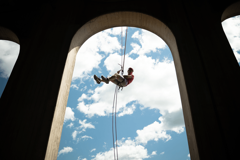 person attached to rope rappelling from under stadium archway