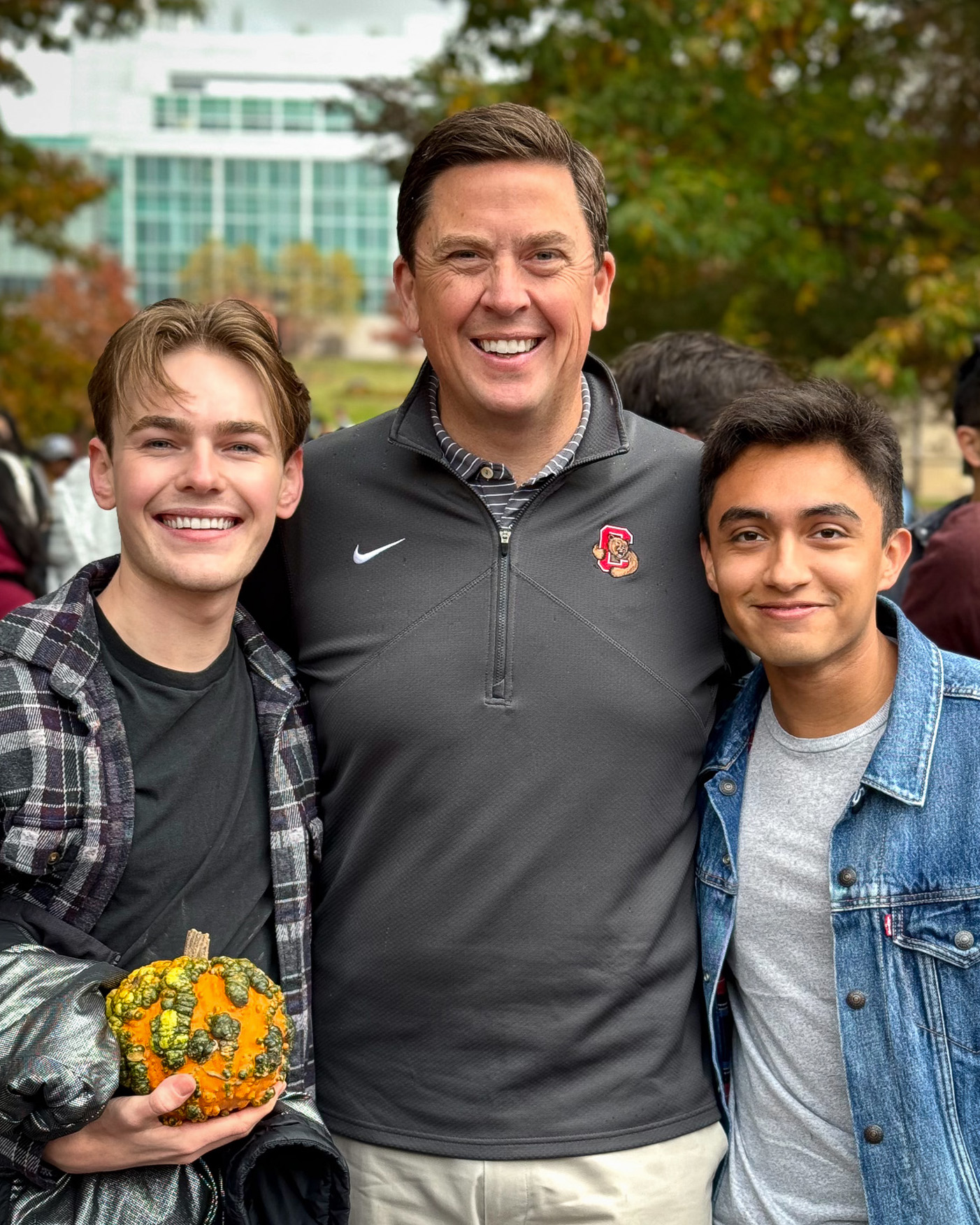 Ryan Lombardi standing with two students. One of the students is holding a pumpkin.