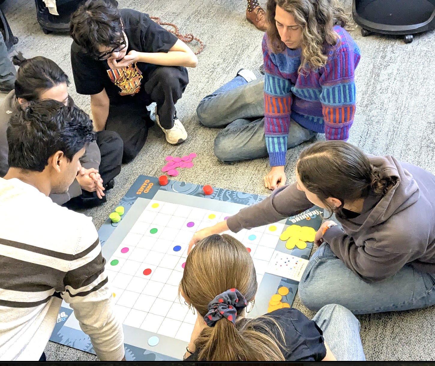 6 people sitting on the floor around a grid with colored dots