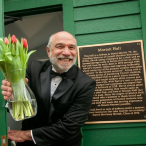 Dave Moriah holding tulips in a glass vase and exiting a green building with Moriah Hall sign on the right.