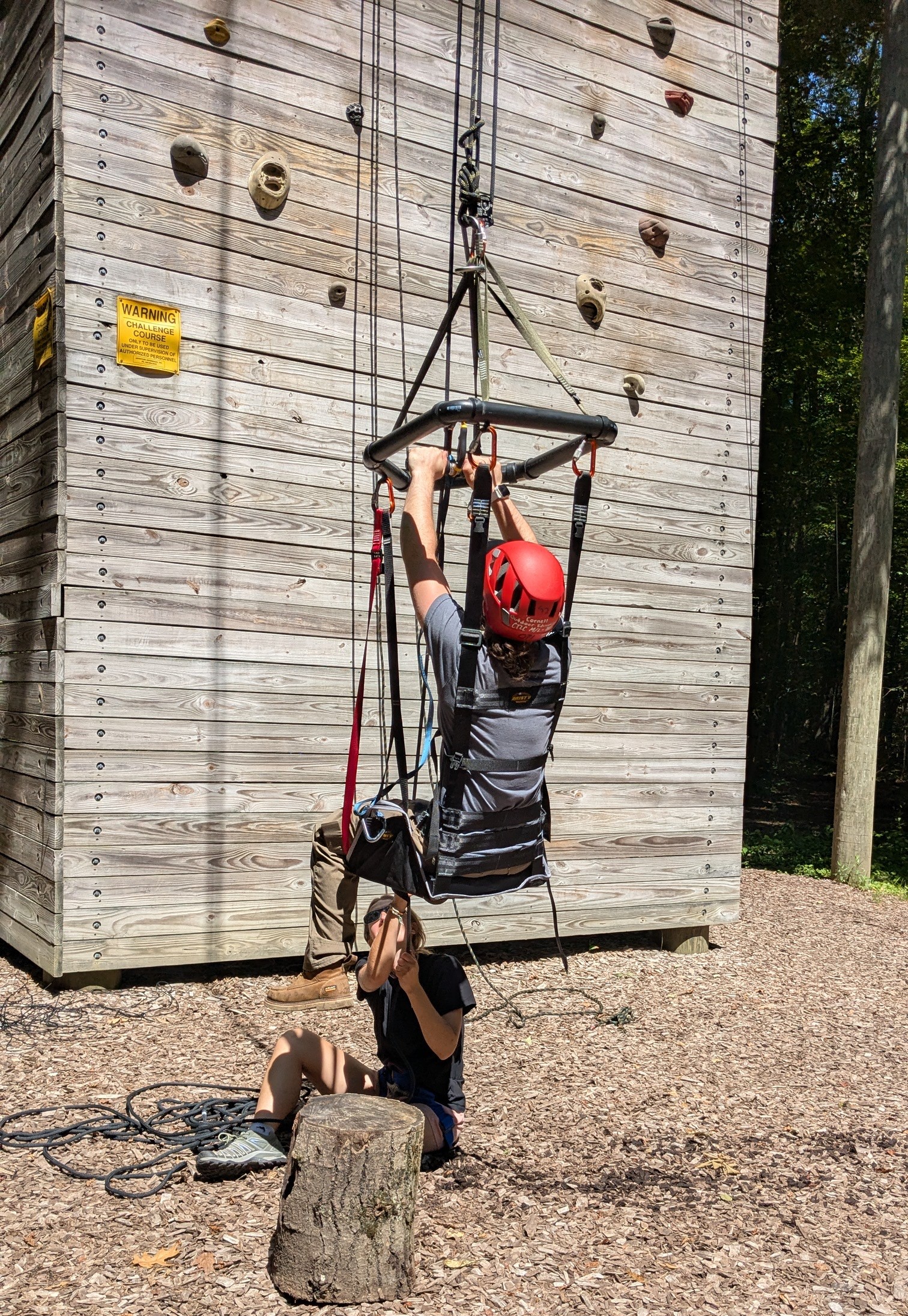 person in suspended ARC harness raising themself off the ground with wooden tower structure in the background