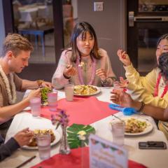 People sit around a dining room table with plates of food. They're each wearing leis around their necks.