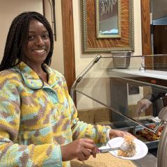 A person stands in front of a food serving line holding a plate