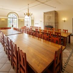 A large dining room with two long tables with chairs on either side and large windows on the far wall.