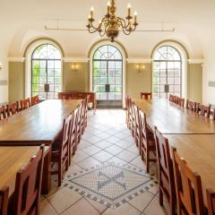 A large dining room with two long tables with chairs on either side and large windows on the far wall.