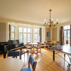 A large lounge with a grand piano, tables, chairs, and a ping pong table.