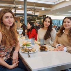 Three young women sitting at a dining room table with plates of food