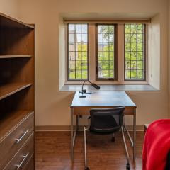 Single room with a bed, desk and chair, drawers, an armoire and a window.
