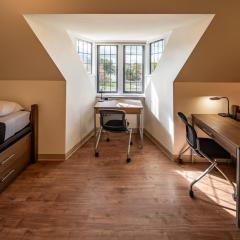 room showing one bed and desk and chair in front of a window and another desk and chair.