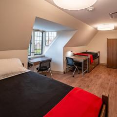 Double room with two beds, two desks and chairs, two sets of drawers, two armoires and a window.