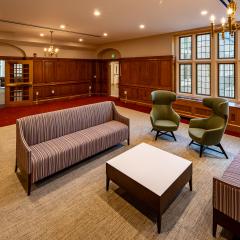 Lounge with two couches and lounge chairs facing a coffee table in a room with wood panelling and windows. 
