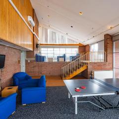 a large roof top lounge with multiple couches and lounge chairs, a tv, a ping pong table, and large windows.