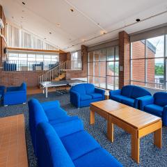 a large roof top lounge with multiple couches and lounge chairs, a tv, a ping pong table, and large windows.