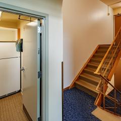 A hallway with stairs that lead up to two suites and stairs that lead down to two suites. There is also a door open to a small communal kitchen featuring a white fridge and shelves.