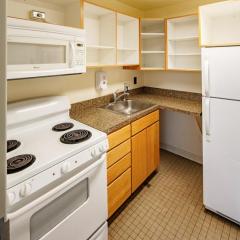 A small kitchen with a stove, countertops, sink, fridge, microwave, and shelves.
