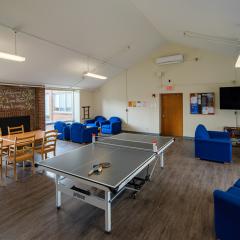 Large lounge with a ping pong table, multiple blue lounge chairs a tv, a long table and chairs, and a fireplace.