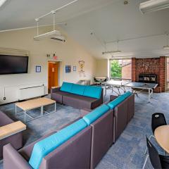 Large lounge with a ping pong table, multiple blue and grey couches a tv, two round tables with chairs, and a fireplace.