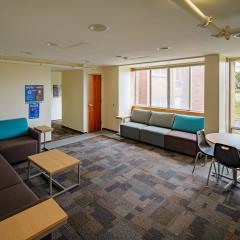 Large lounge with three multi-colored couches, a round table with chairs, and a large window.