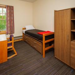 A bedroom in with a twin bed, dresser, desk, and chair.