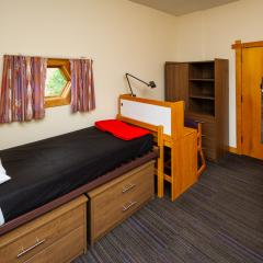 A bedroom in with a twin bed, dresser, desk, and chair.