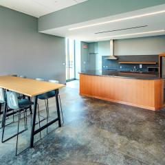 A close up of the large communal kitchen with cabinets and countertops, a sink, a fridge, a microwave, a stove, and a high top table with chairs, in Barbara McClintock Hall.