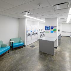 the laundry room in Barbara McClintock Hall, featuring many washers and dryers, a table to fold clothes, and two chairs with a small table attached. 