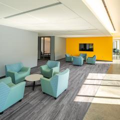A large sitting area with grey striped carpet, blue lounge chairs, circle tables and a tv. 