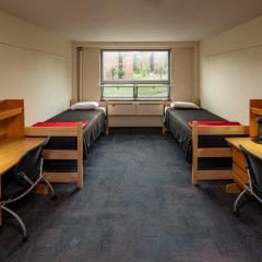 Double room with two beds, sets of drawers, desks and chairs, and a window.