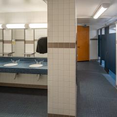 A bathroom with three sinks and mirrors and a hallway of three showers.