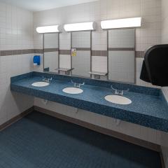 Three bathroom sinks on blue countertops with three mirrors and a paper towel dispenser.