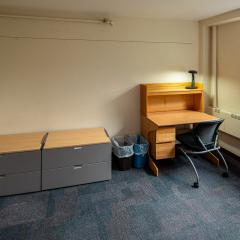 Single room with drawers, a desk, a chair, and a window.