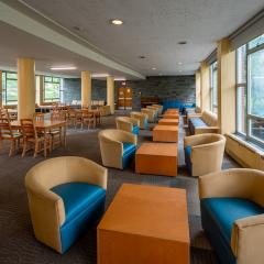 Large room with many lounge chairs and tables with chairs and large windows on both sides of the room.