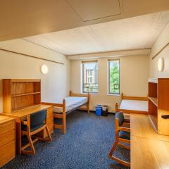 Double room with two beds, two desks and chairs, two sets of drawers, and a window.