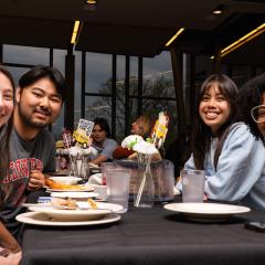 Four people around a dining table smile towards us