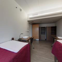 Double room facing the door showing the end of two beds, two desks and chairs, two armoires and the door to the room.