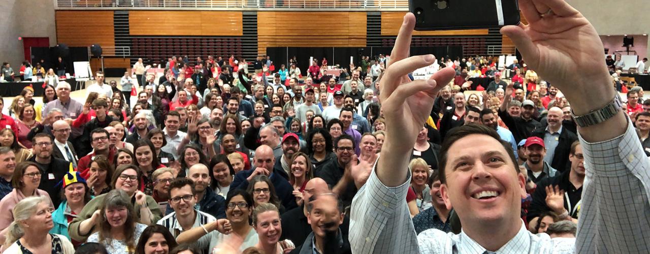 Ryan Lombardi taking a selfie with the SCL staff in the background inside of Bartels Hall