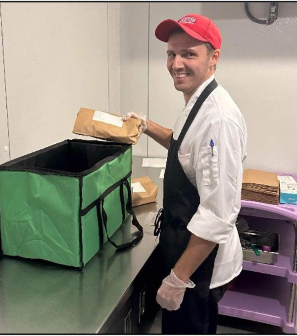 A smiling person in an apron places a paper-wrapped item in a large open cooler
