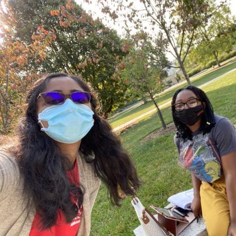 Student Peer Ambassador distributes mask and safety supplies to a student sitting on a bench on campus