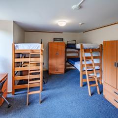 A triple room with two lofted beds, one lower bed, a desk, chair, and three armoires, on blue carpet with one window. 